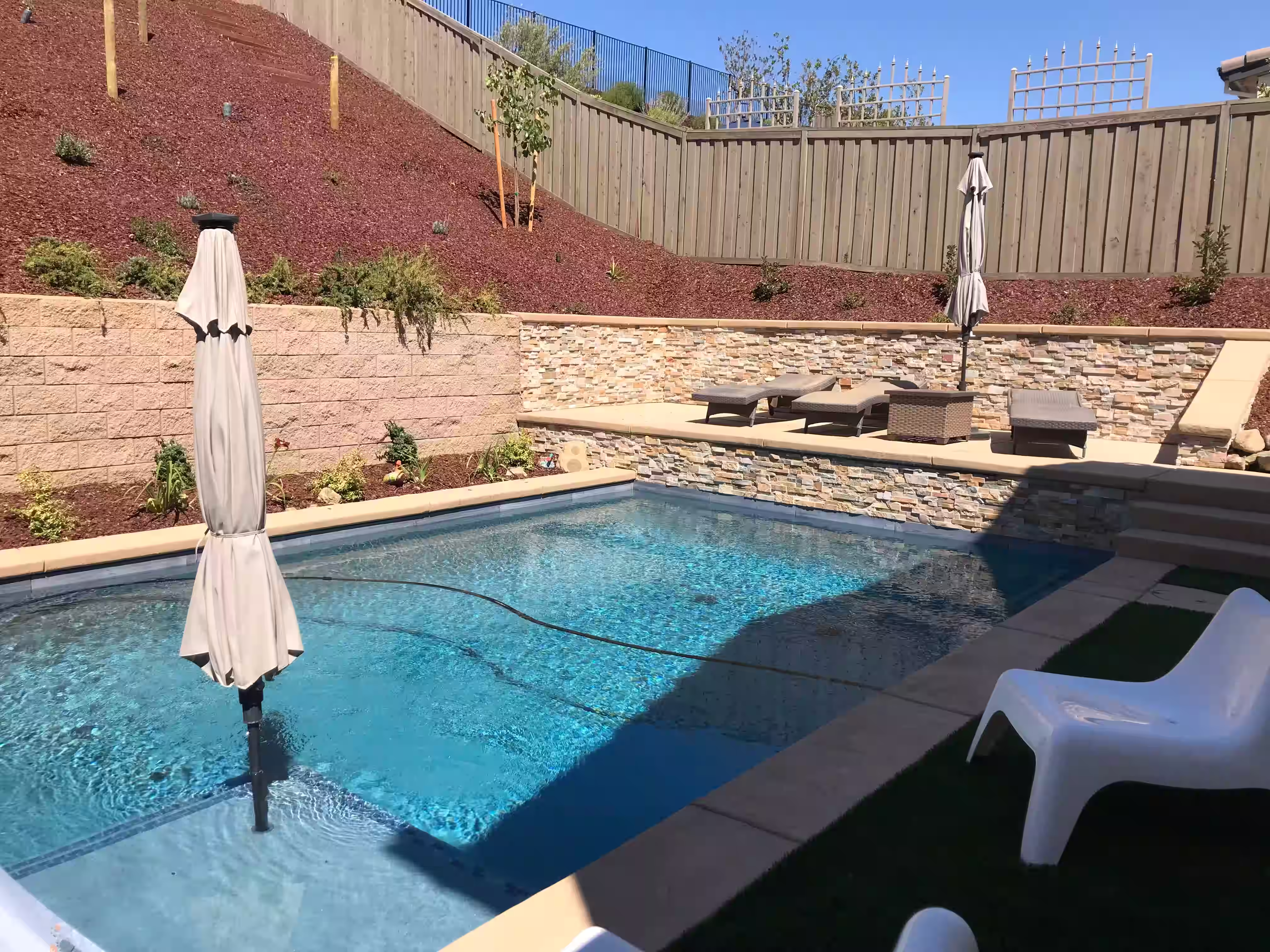 Poolside landscaping that integrates retaining walls, hillsies, and lounge areas